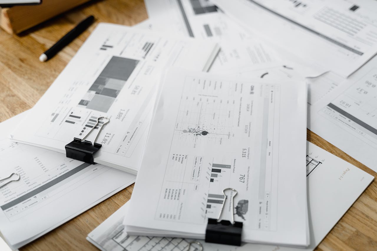 about-us-02 A stack of financial reports and graphs with clips on a wooden desk, highlighting business planning.